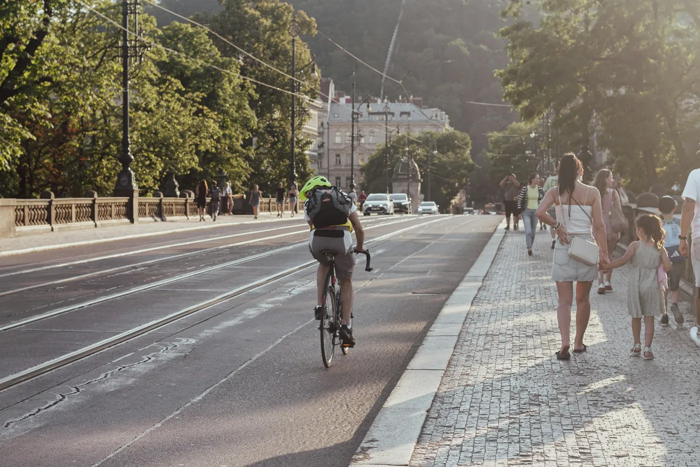 Radfahrer auf einer Prager Brücke mit Straßenbahngleisen, daneben Fußgänger