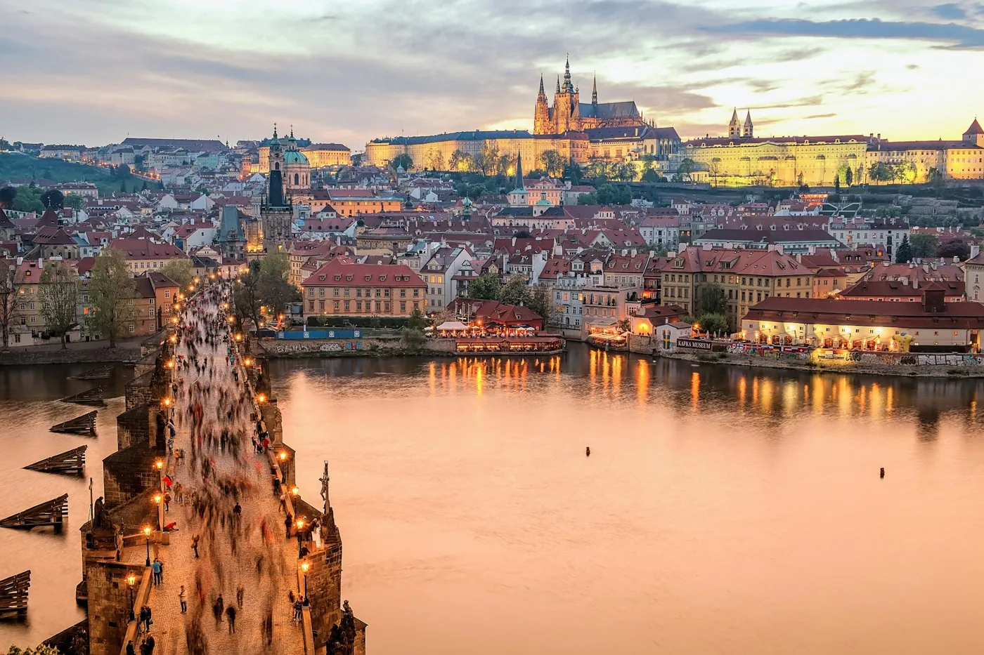 Karlsbrücke mit Statuen und Laternen im Abendlicht, dahinter Kleinseite und Prager Burg, vom Altstädter Brückenturm aus gesehen