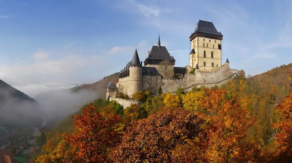 Burg Karlštejn im Herbst mit Kaiserpalast und Großem Turm über bunten Wäldern