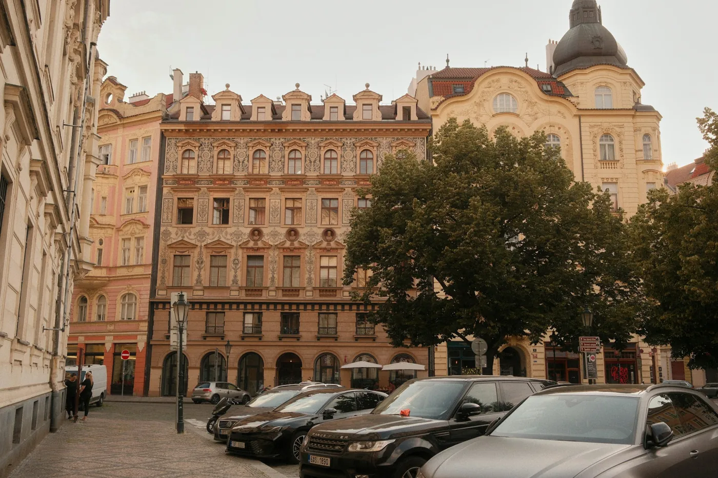 Geparkte Autos auf einer Kopfsteinpflasterstraße vor Altbauten in Prag