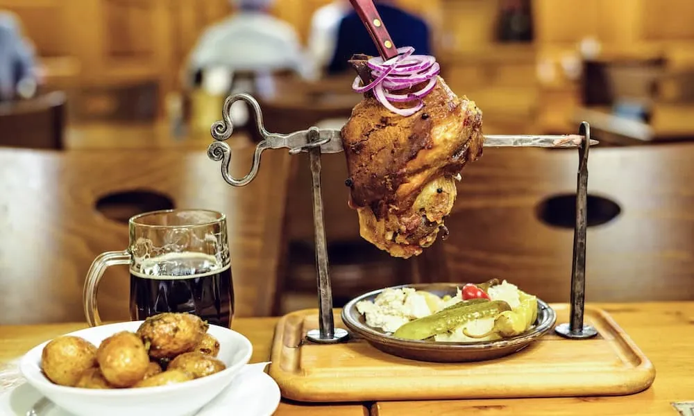 Gebratenes Schweineknie am Spieß mit Kartoffeln, Essiggurken und dunklem Bier in einer Prager Gaststätte
