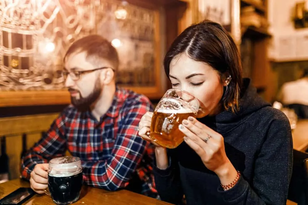 Zwei Gäste mit Bierkrügen, helles und dunkles Bier, an einem Holztisch in einer Prager Kneipe