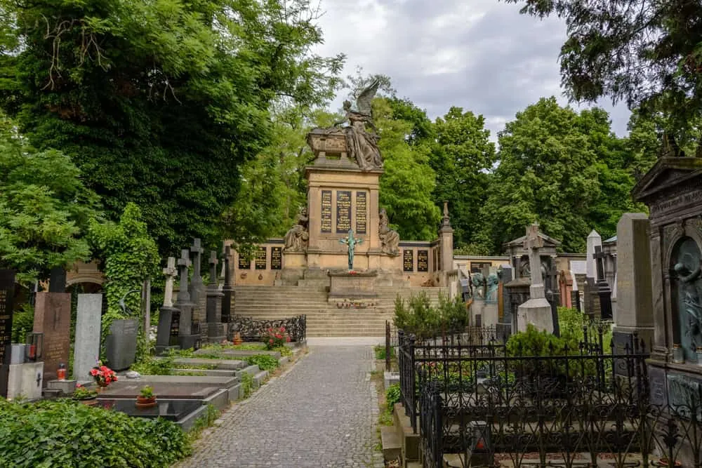 Weg zwischen Gräbern auf dem Vyšehrader Friedhof mit Denkmal und Bäumen