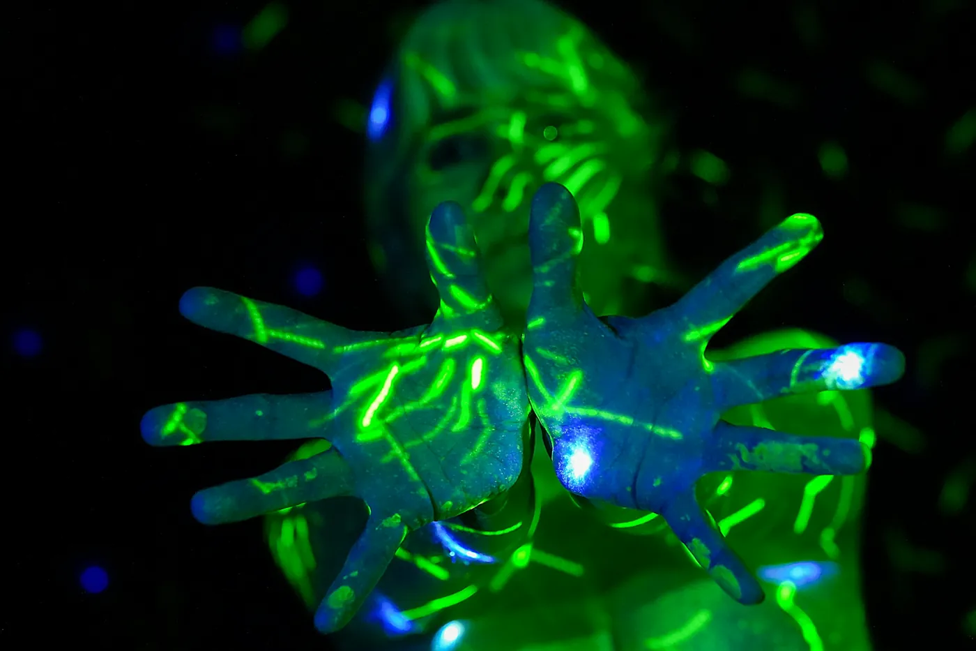 Hände mit leuchtender grüner Farbe unter UV-Licht vor schwarzem Hintergrund
