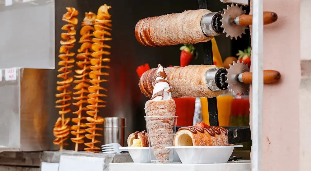 Trdelník-Teigrollen auf Spießen über der Glut an einem Stand