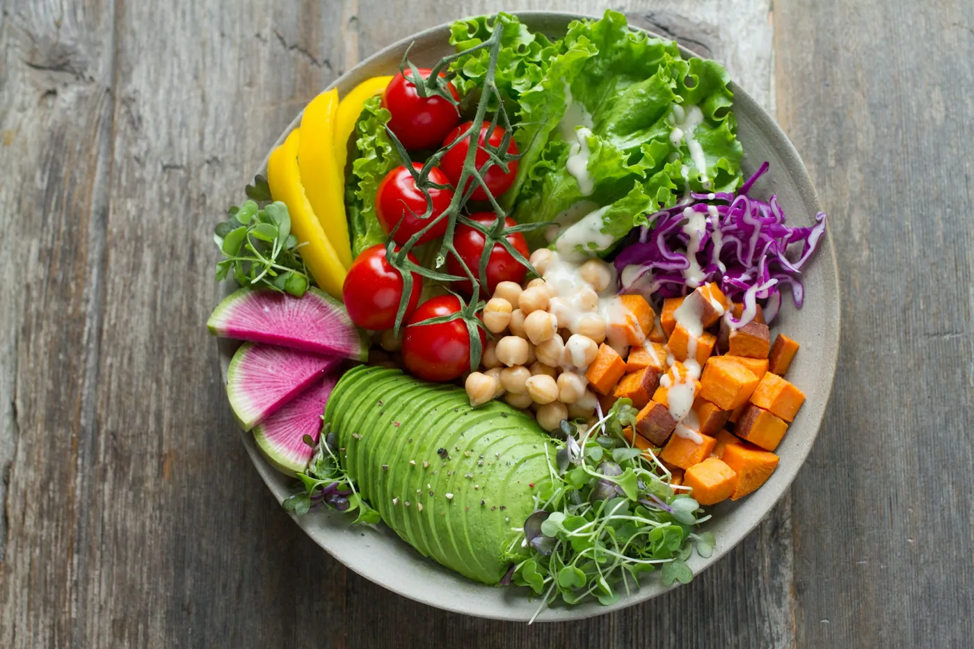 Schale mit Avocado, Kichererbsen, Tomaten, Süßkartoffel und Rotkohl auf einem Holztisch