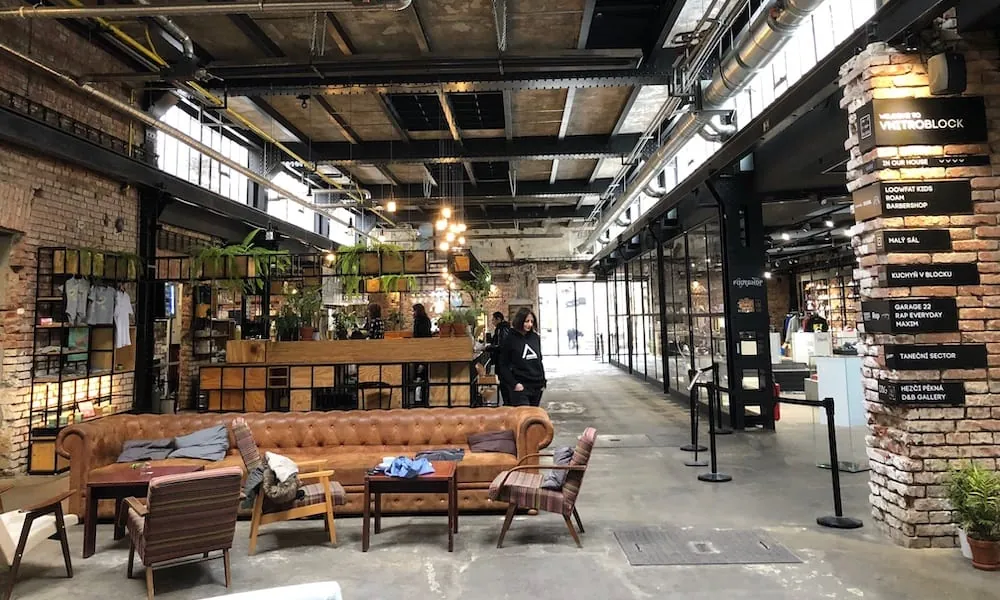 Vnitroblock in Holešovice: Industriehalle mit Café, Sofas und Ziegelsäulen
